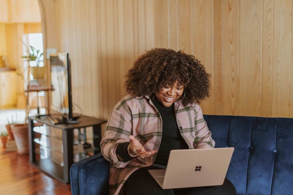 Woman smiling and sitting on a couch using a laptop